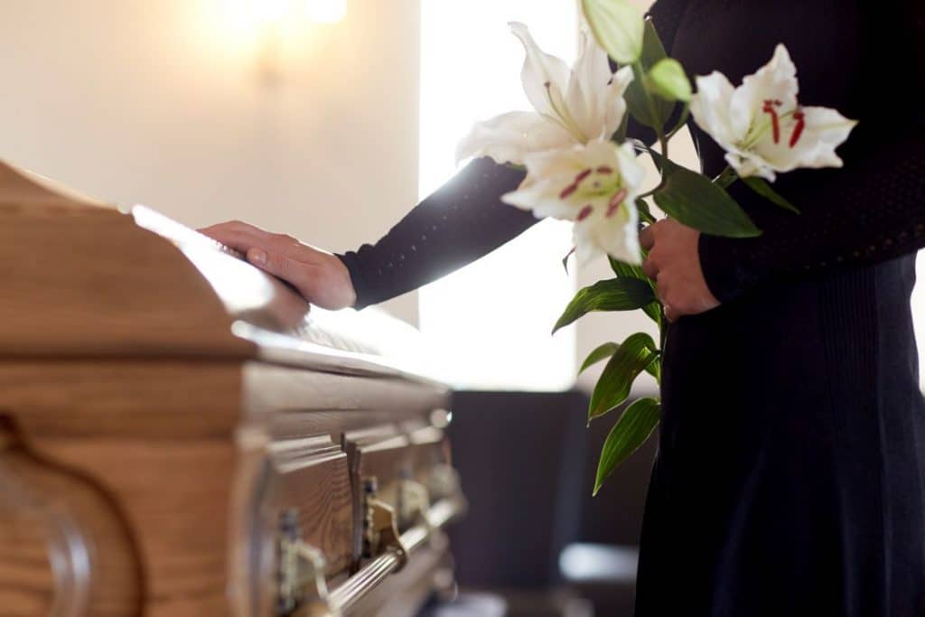 woman with lily flowers and coffin at funeral 1024x683 - The Art of Comfort: The Many Ways Funeral Directors in Singapore Support the Bereaved