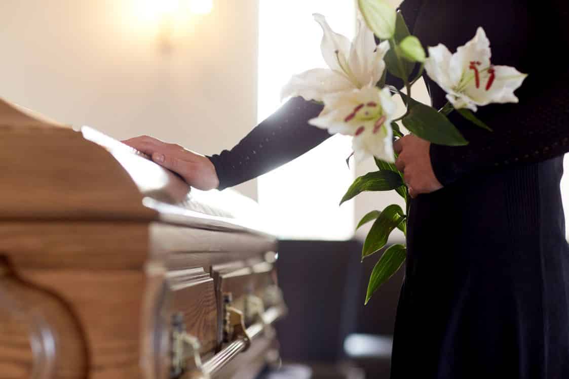 woman with lily flowers and coffin at funeral - International Repatriation